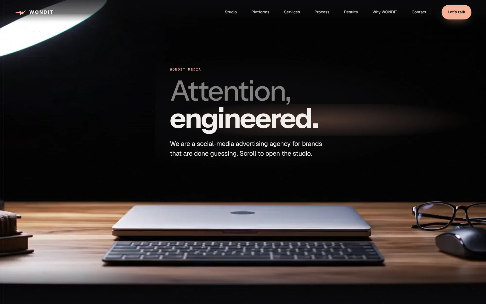 WONDIT Media homepage: the headline Attention, engineered. above a closed laptop on a wooden desk under a lamp.